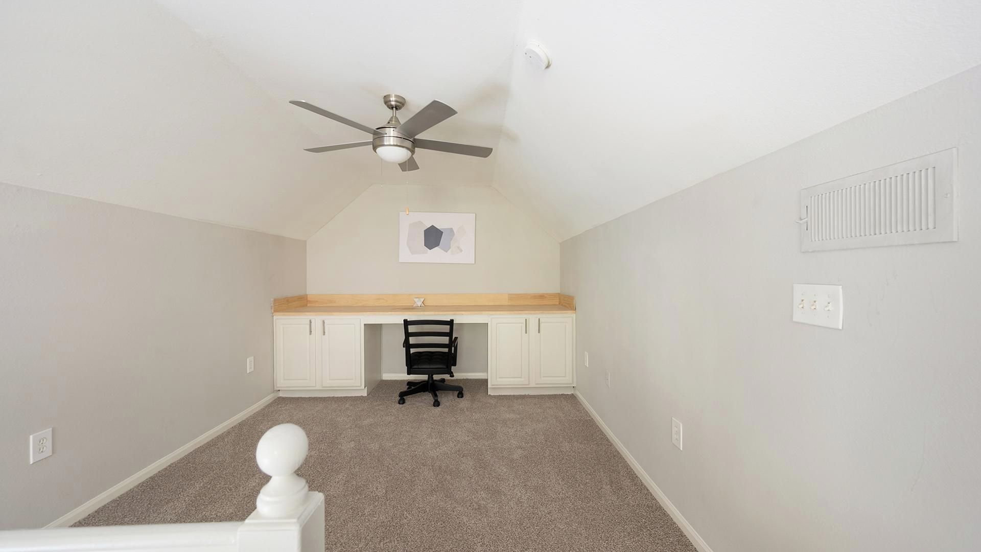 Une chambre à coucher avec un ventilateur de plafond, un bureau avec une chaise et un tableau encadré au mur.