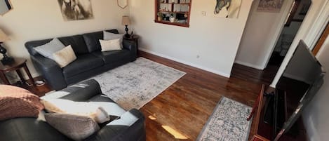 A living room with a black leather sofa, a wooden coffee table, and a patterned rug.
