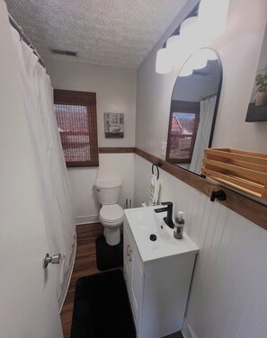 A compact bathroom with a toilet, sink, and mirror. - Lovely 2-bedroom house with AC in cool Russell (Russell)