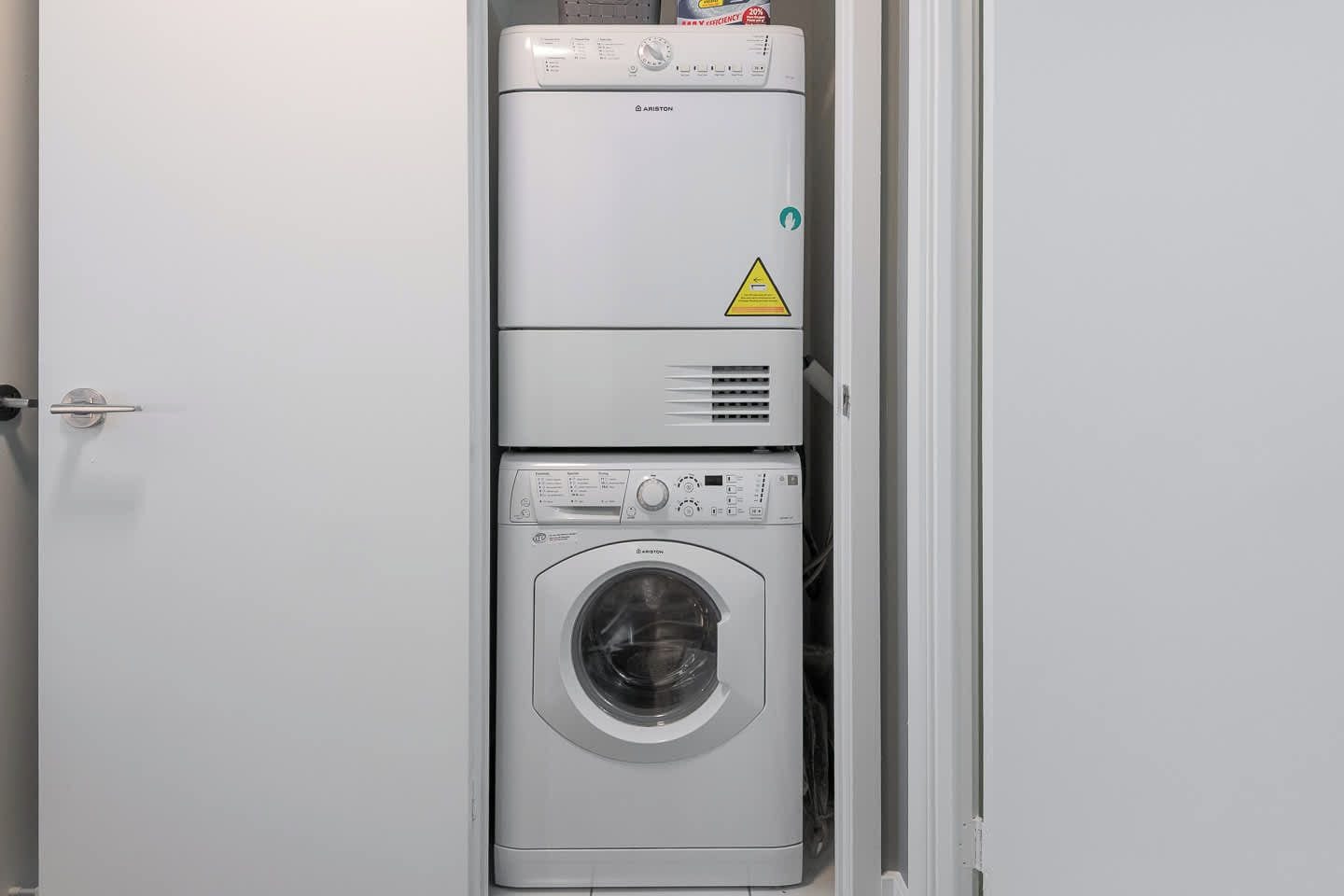 A compact, white, wall-mounted washer and dryer unit with a control panel and a warning label.