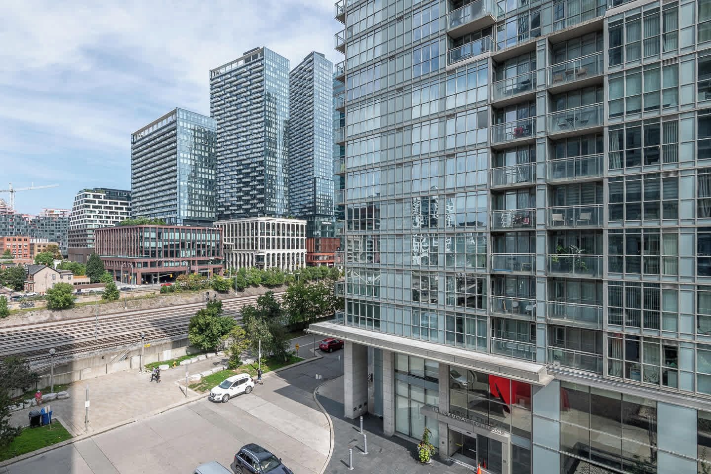 A modern building with a glass facade, a parking area, and a train track in the foreground.