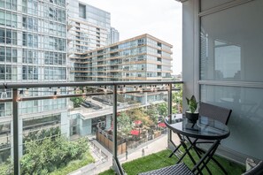 Ein Balkon mit Glastrennung, Tisch und Stuhl mit Blick auf eine Stadtlandschaft aus modernen Gebäuden und einem Park.