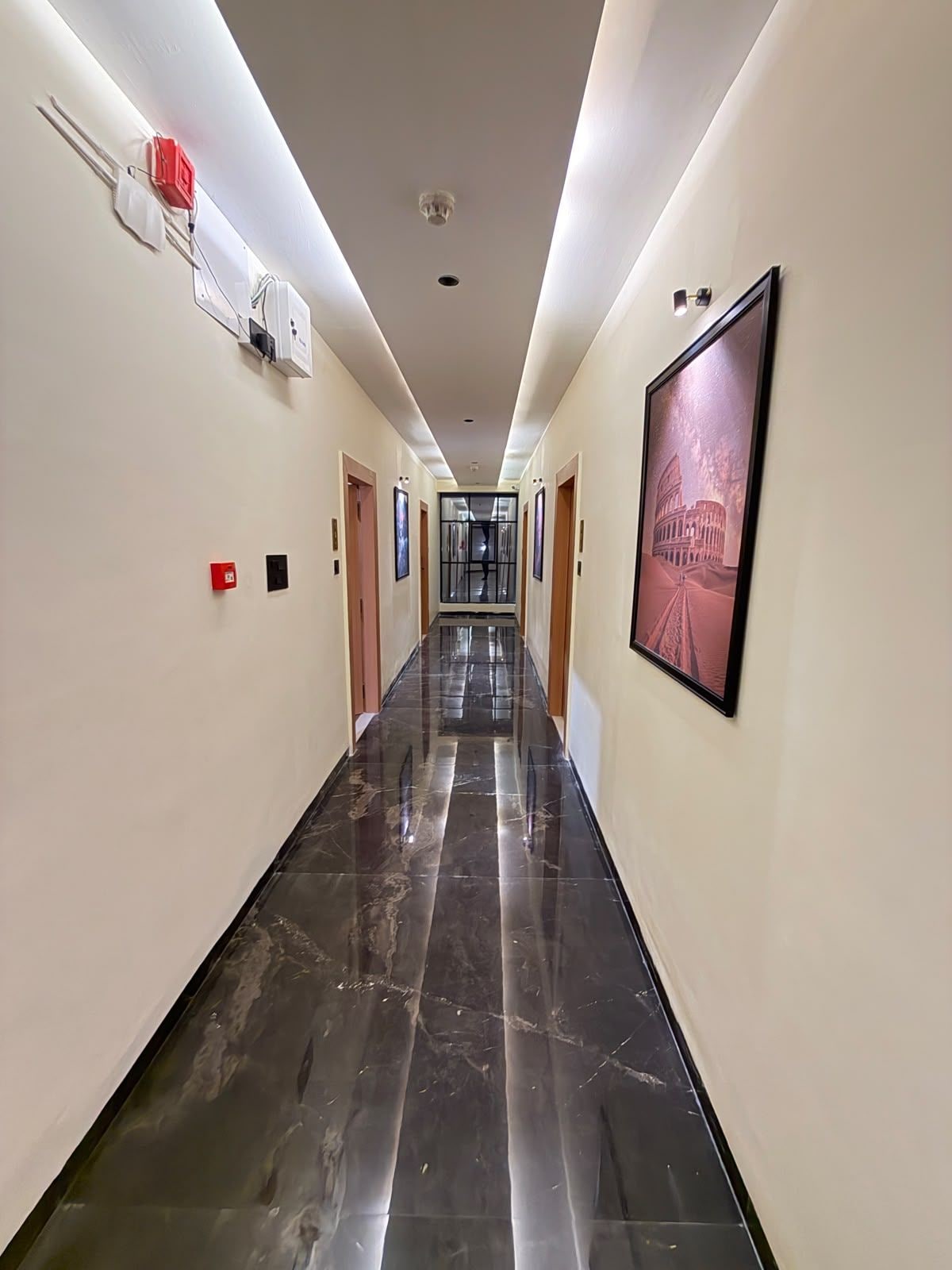 A hotel hallway with a polished marble floor, framed pictures on the walls, and a clear view to the end of the corridor.
