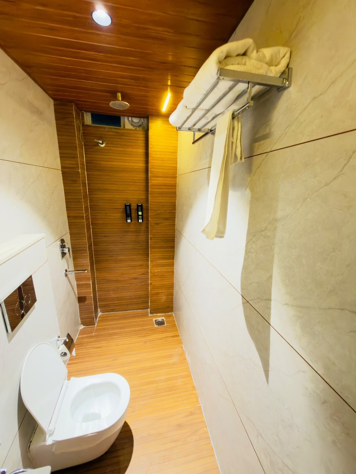 A modern bathroom with a wooden ceiling, a toilet, a shower area, and a towel rack.