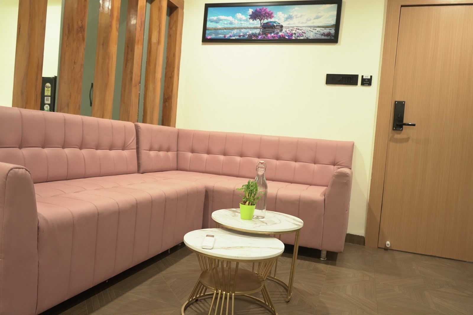 A pink sofa, a small round table with a bottle and a plant, and a door with a lock.