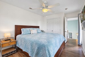 A bedroom with a bed, a nightstand, a ceiling fan, and a door leading to another room.