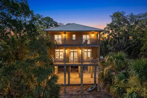 A two-story wooden house with a balcony, surrounded by dense vegetation. - Crosswinds Cottage - Private Waterfront Escape Off The Runway + Golf Cart (Cedar Key)