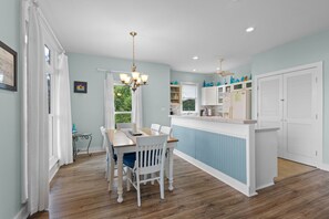 A modern kitchen with a dining area, wooden flooring, and a view of greenery outside. - Crosswinds Cottage - Private Waterfront Escape Off The Runway + Golf Cart (Cedar Key)