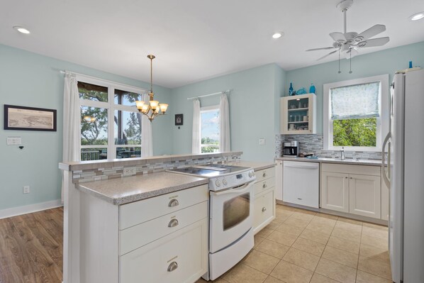 A modern kitchen with a central island, white cabinetry, a built-in oven, and a ceiling fan.