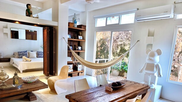 Un salon moderne avec une table à manger en bois, un hamac et une grande fenêtre donnant sur l’extérieur.