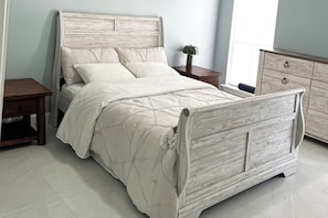 Ein Bett mit Kopfteil, ein Nachttisch, eine Kommode und ein Fenster mit Vorhängen.