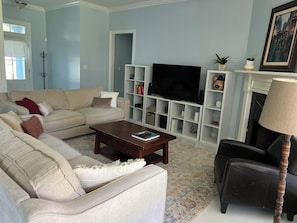 Ein Wohnzimmer mit einem beigefarbenen Sofa, einem Couchtisch, einem schwarzen Sessel, einem Fernseher und einem Kamin.
