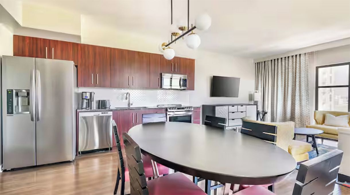 Una cocina moderna con electrodomésticos de acero inoxidable, un comedor con una mesa redonda y una sala de estar con sofá y televisor.