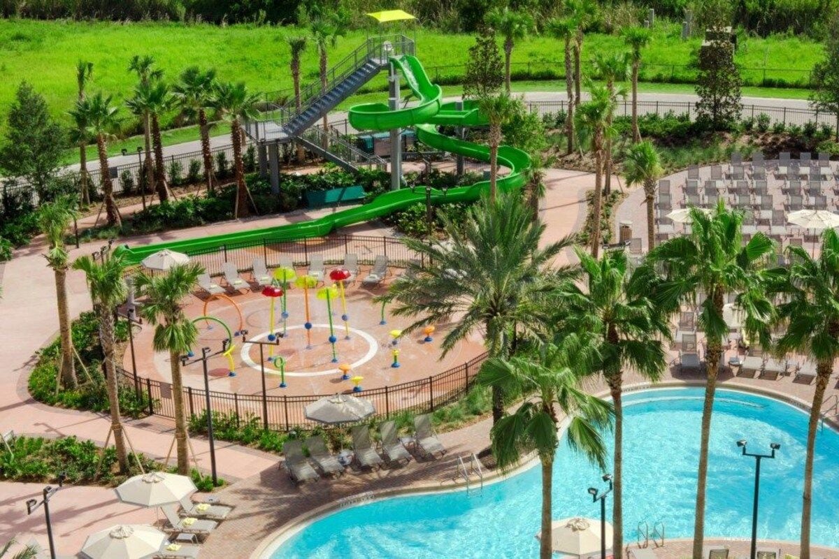A pool area with a water slide, lounge chairs, and palm trees.