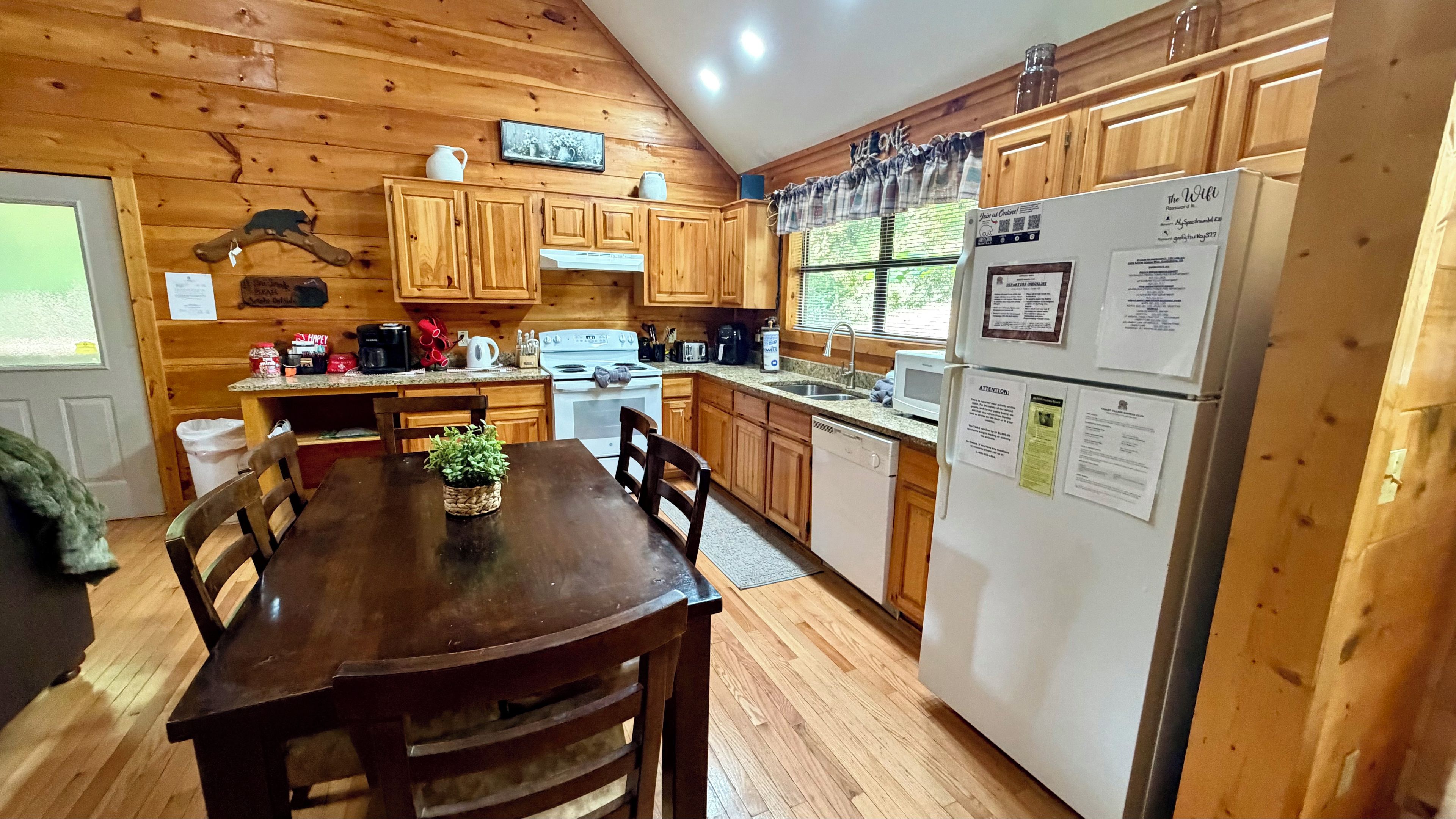 A wooden cabin-style kitchen with a dining table, chairs, a refrigerator, and wooden cabinets.
