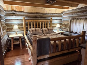 Une chambre dans un chalet en rondins, avec un lit en bois, deux tables de chevet et une fenêtre avec des rideaux.