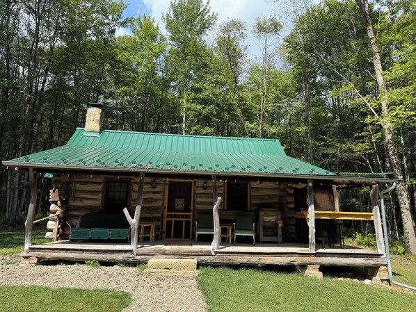 A log cabin with a green metal roof, a porch with seating, and a wooden deck. - Rustic Charm meets Woodland Peace • Where every sunrise is a blessing (Pleasantville)