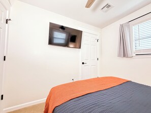 A bedroom with a bed, a television mounted on the wall, a door, and a window with blinds.