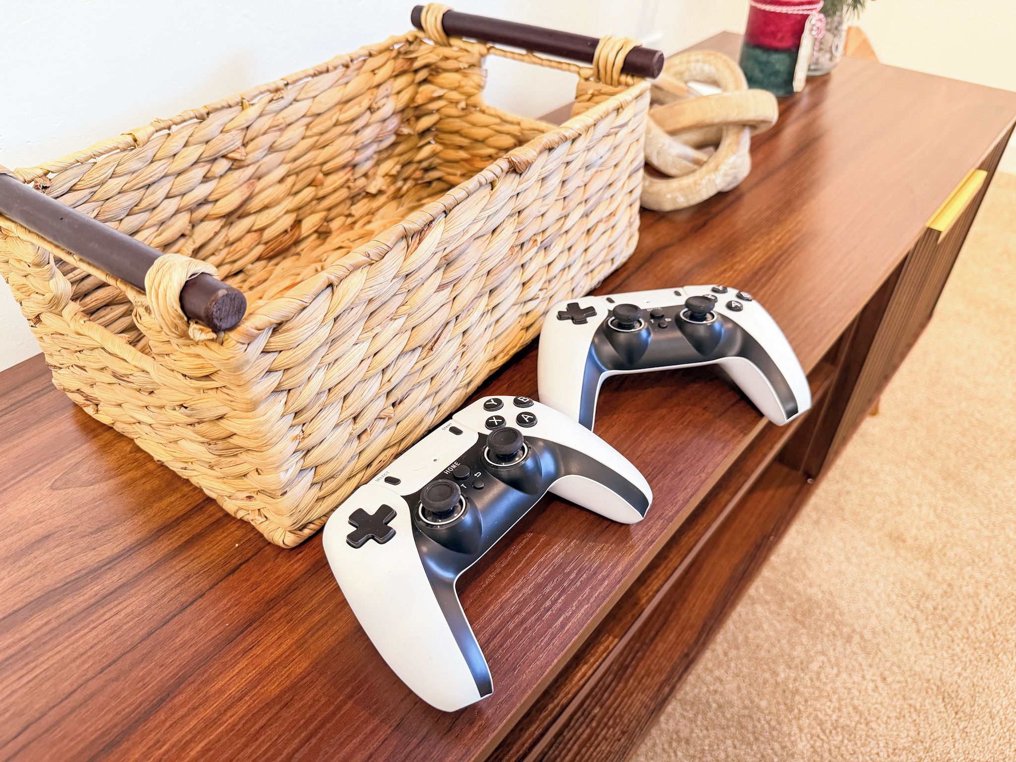 Un panier tressé avec des anses, deux manettes de jeu et un objet en bois sur une table en bois.