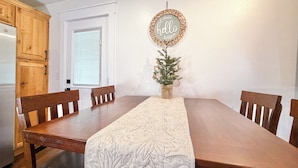 Un comedor con una mesa de madera, cuatro sillas, un camino decorativo, un letrero que dice 'hello' y un pequeño árbol de Navidad.