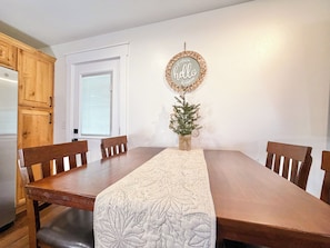Un coin repas avec une table en bois, quatre chaises, un chemin de table décoratif, un panneau indiquant « Bonjour » et un petit sapin de Noël.