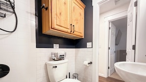 Un baño con inodoro, bañera, lavamanos y armarios de madera sobre el inodoro.