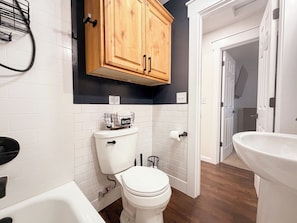 Une salle de bain comprenant des toilettes, une baignoire, un lavabo et des meubles en bois au-dessus des toilettes.
