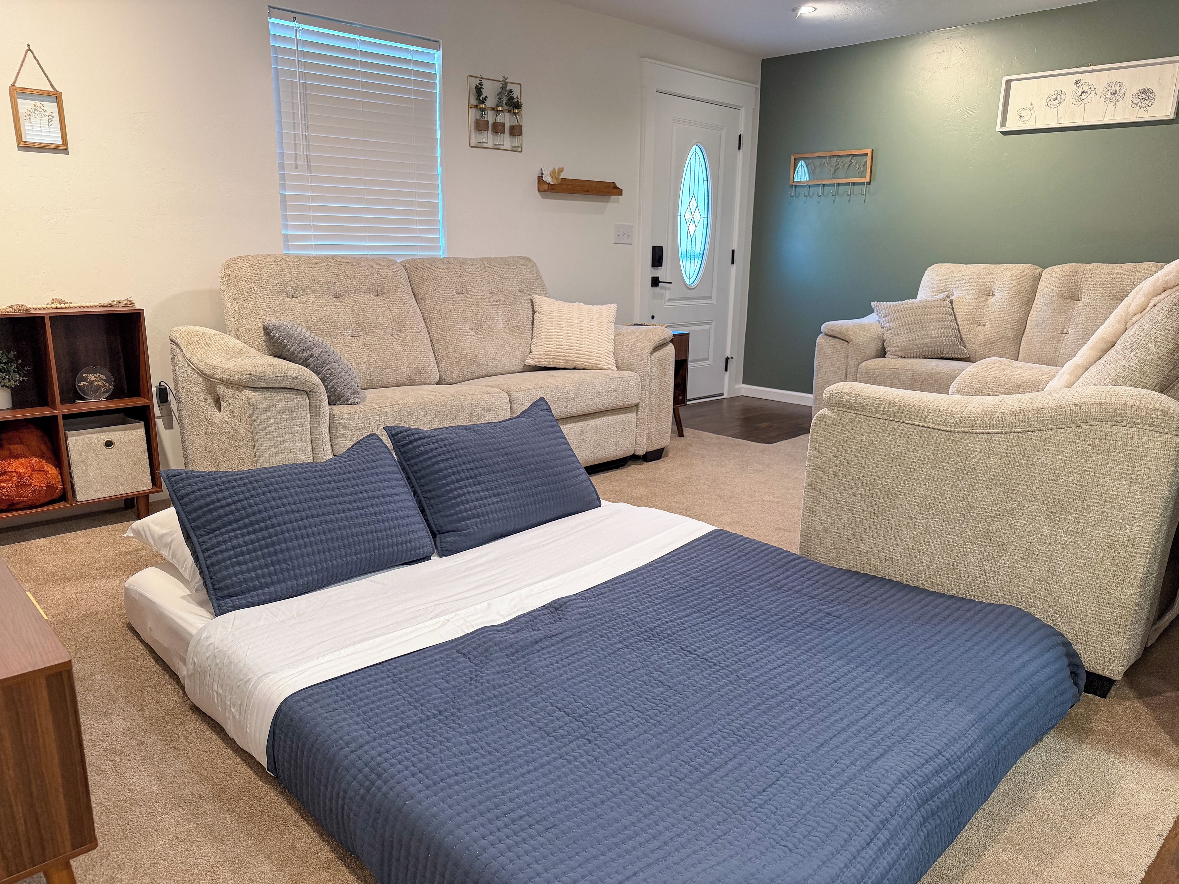 Ein Schlafzimmer mit einem Bett, zwei Sofas, einem Holznachttisch und einem an der Wand befestigten Regal.