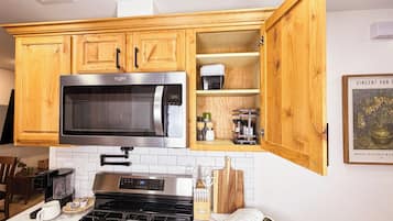 Une cuisine avec des meubles en bois, un four à micro-ondes en acier inoxydable, une cuisinière et un plan de travail sur lequel se trouvent une machine à café et des ustensiles.