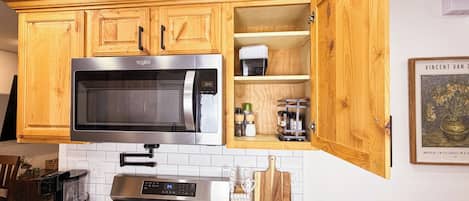 A kitchen with wooden cabinets, a stainless steel microwave, a stove, and a countertop with a coffee maker and utensils.