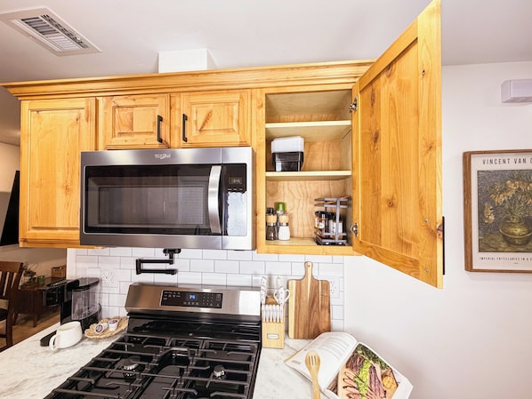 A kitchen with wooden cabinets, a stainless steel microwave, a stove, and a countertop with a coffee maker and utensils.