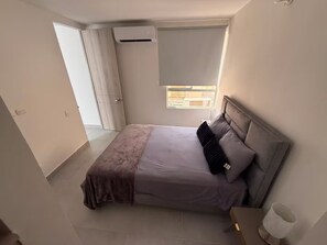 A bedroom with a bed, a bedside table, an air conditioning unit, and a window. - Welcome to MA Cartagena • Playa • Piscina (Bolívar)