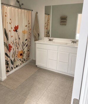 Un baño con cortina de ducha con estampado floral, un lavabo blanco con un espejo arriba y una toalla beige colgada en la pared.