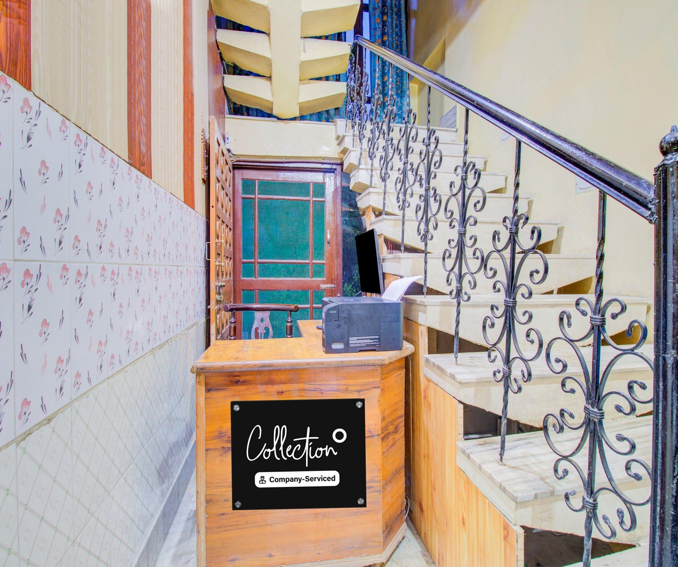 A staircase with ornate metal railings, a wooden reception desk with a sign, and patterned wall tiles.
