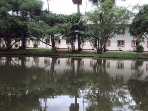 Um lago tranquilo refletindo árvores e um edifício com janelas emolduradas a vermelho.
