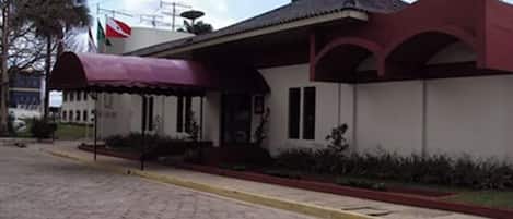 Un edificio con un toldo rojo, una bandera y un área de entrada con baldosas.