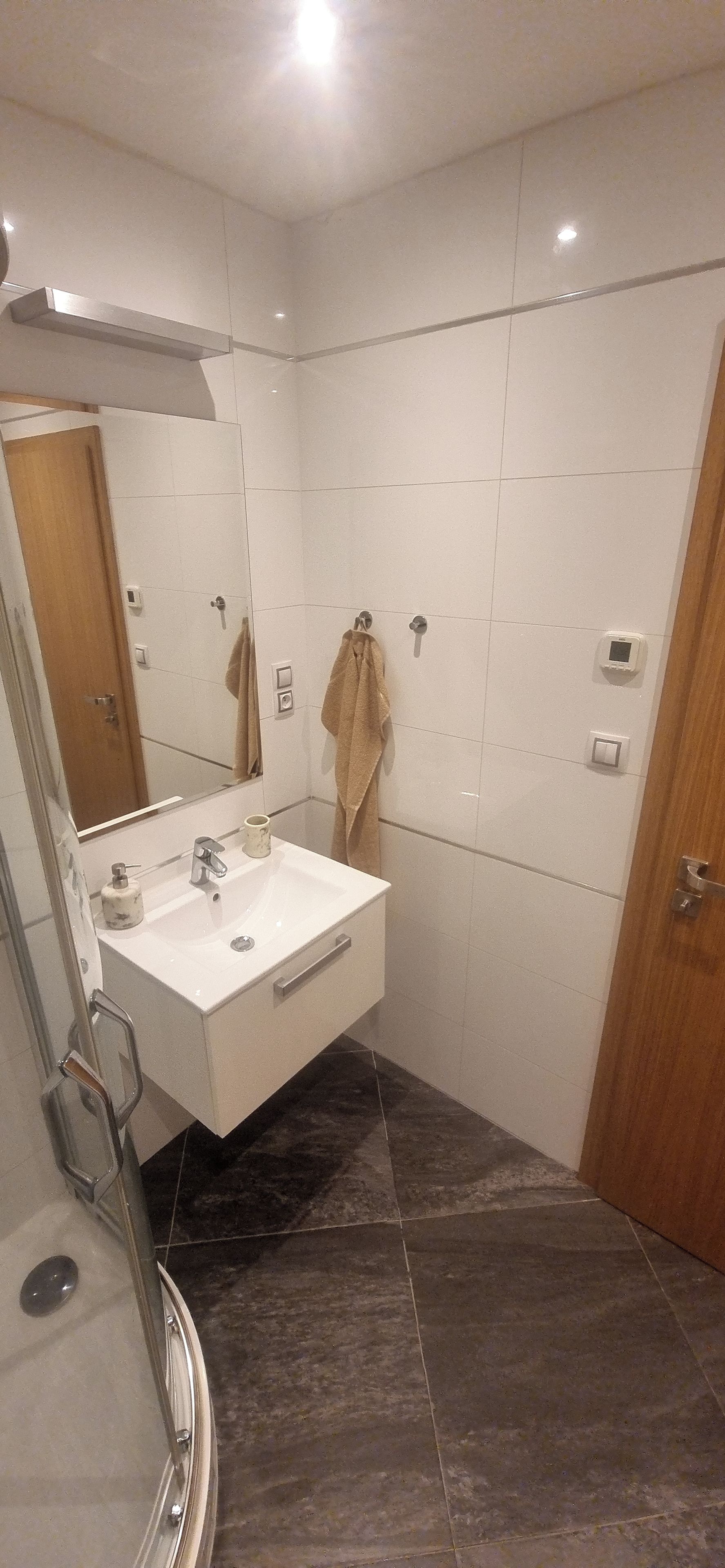 Un baño moderno con un tocador blanco, un espejo, un perchero y una zona de ducha.