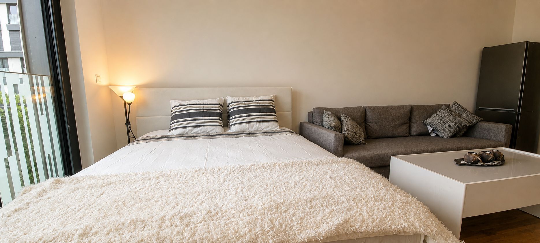 Un dormitorio con una cama, un sofá gris, una mesa de centro blanca y un armario.