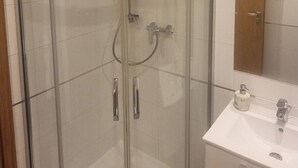 Un baño en esquina con ducha envuelta en vidrio, un lavamanos blanco y un espejo sobre él.