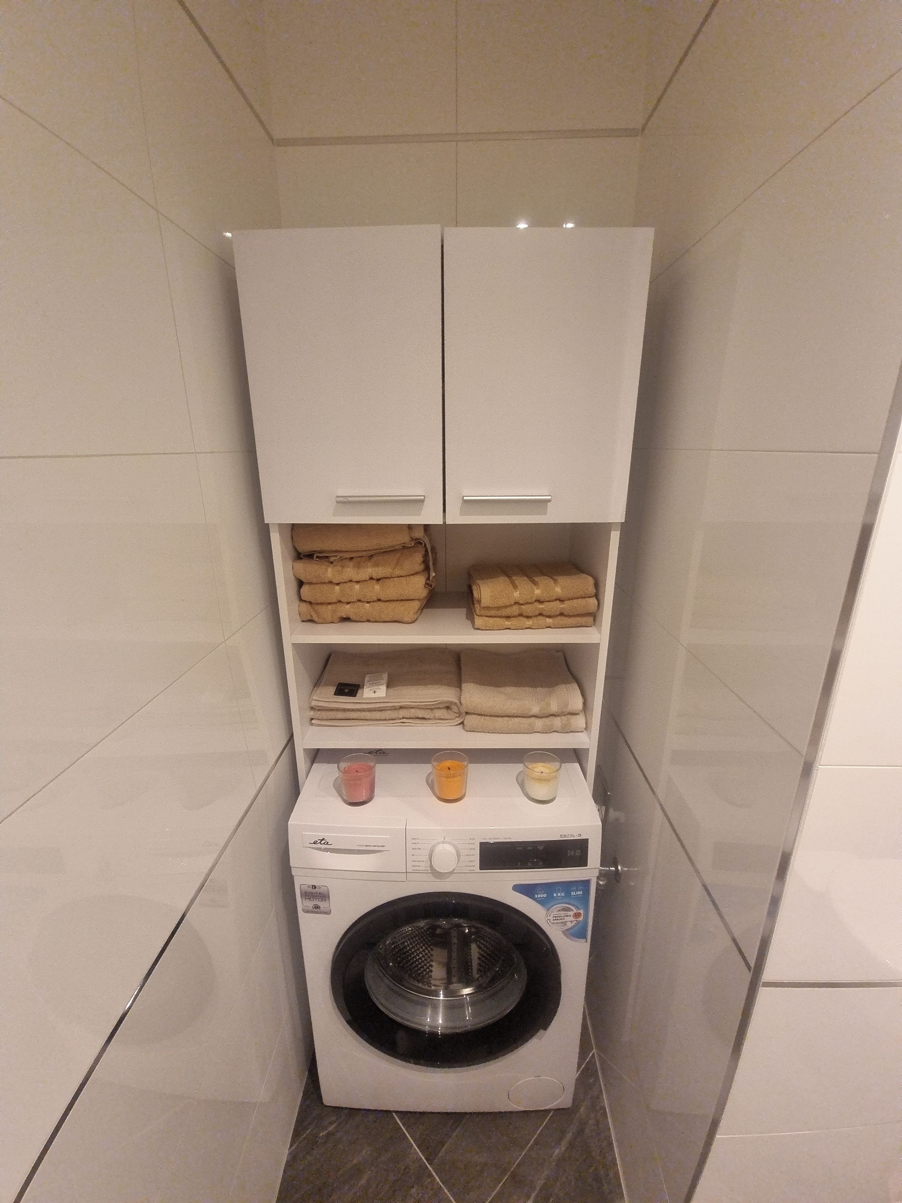 Un lavadero pequeño con lavadora, repisas para toallas y un mueble auxiliar.