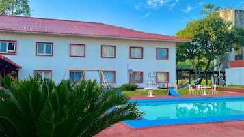 Um hotel com piscina, área gramada e edifício com telhado vermelho.
