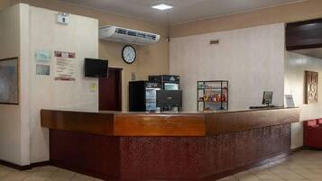 Uma área de recepção com balcão de madeira, relógio, refrigerador e máquina de café.