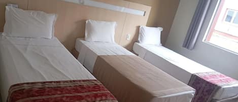 Una habitación de hotel con dos camas individuales, una mesita y un ventanal con cortinas.
