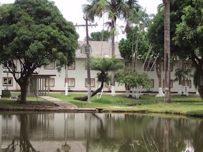 A building with a tiled roof, surrounded by a pond and palm trees. - Convenient Room Near Local Landmarks | Outdoor Pool & Lake Access + Free Parking (Pará)