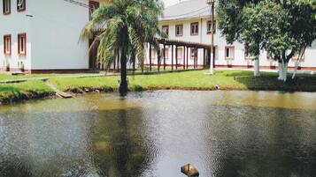 Um edifício com fachada branca e detalhes vermelhos, uma área externa coberta e um lago com um pássaro.