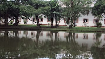 Um lago tranquilo refletindo árvores e um edifício com janelas emolduradas a vermelho.