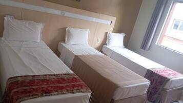 Quarto de hotel com duas camas de solteiro, uma mesa pequena e uma janela com cortinas.
