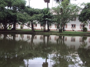 Um lago tranquilo refletindo árvores e um edifício com janelas emolduradas a vermelho.