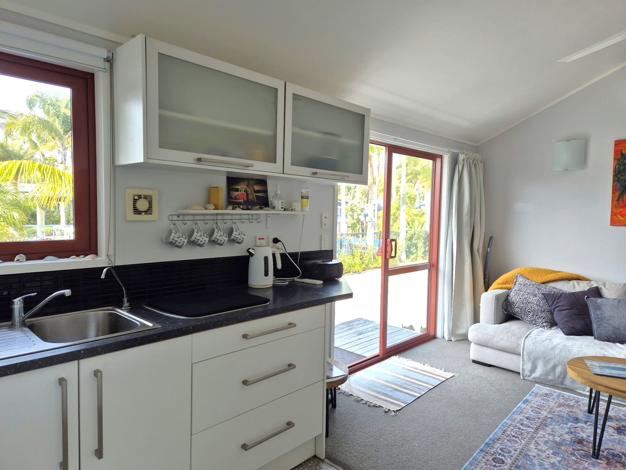 Une cuisine moderne avec un plan de travail noir, des meubles blancs et une porte-fenêtre coulissante donnant sur un balcon.