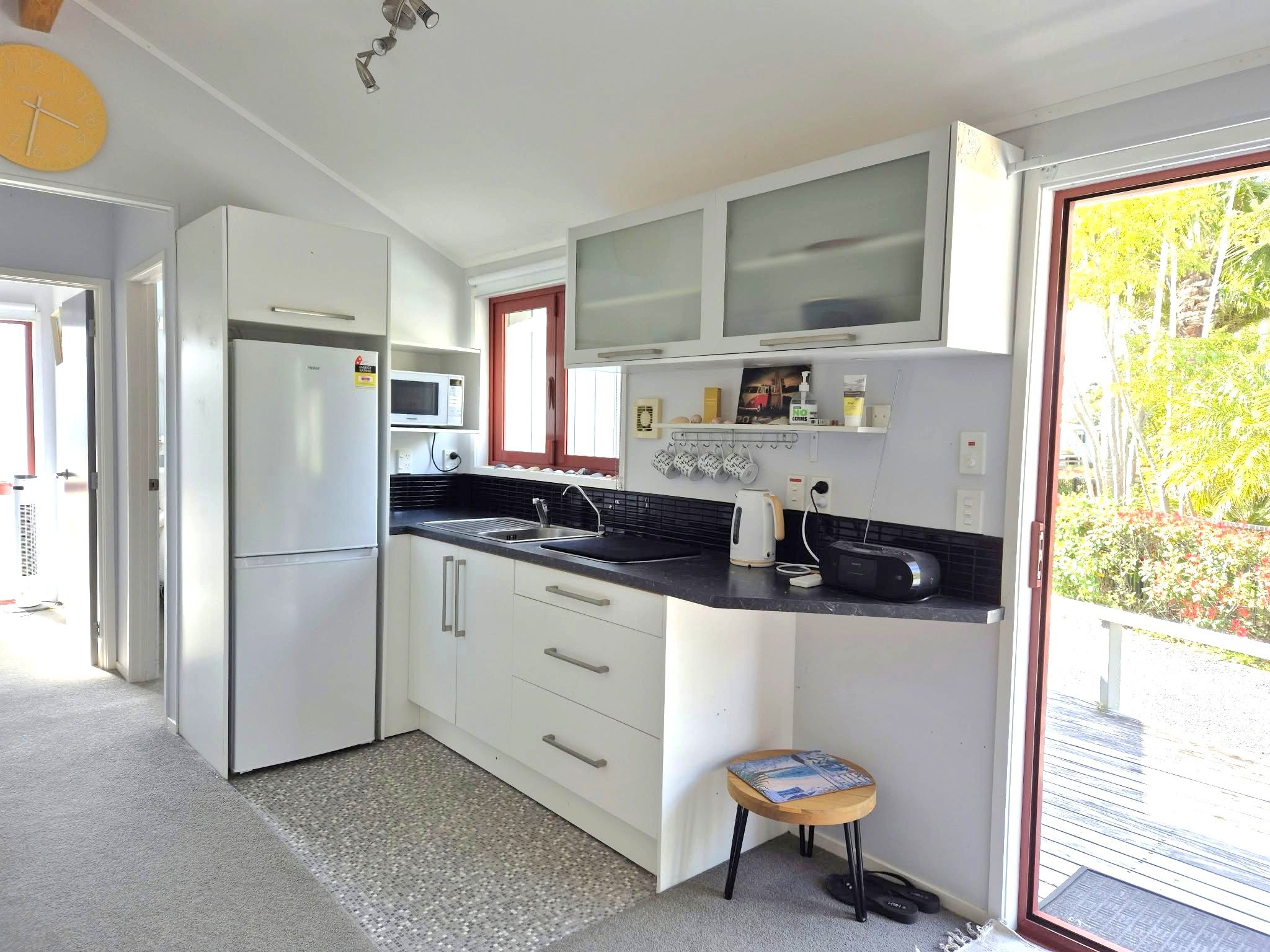 A compact kitchen with white cabinets, a microwave, a sink, and a small stool.